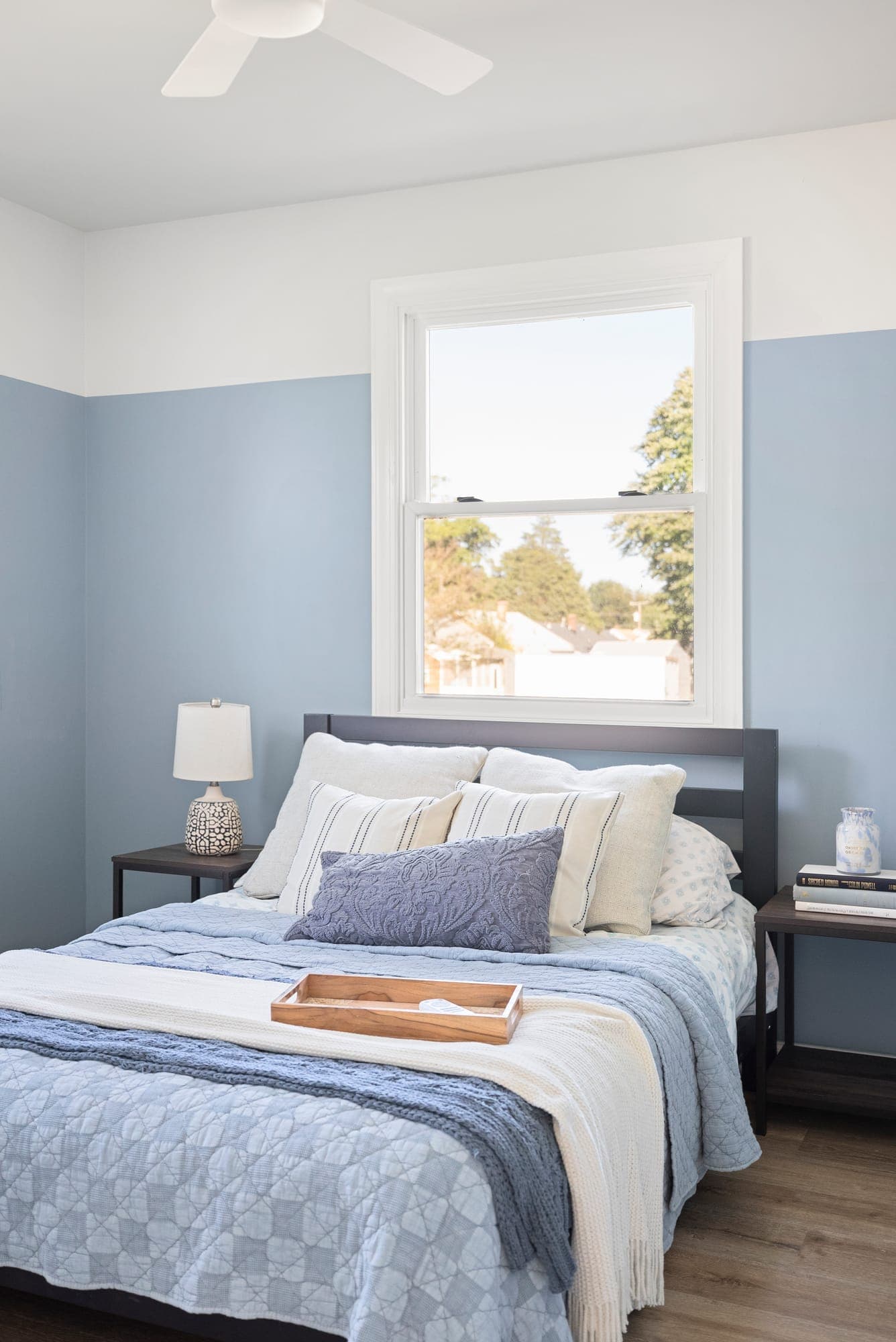 Bedroom painted two-tone, soft blue lower walls under white, with a double-hung window and ceiling fan