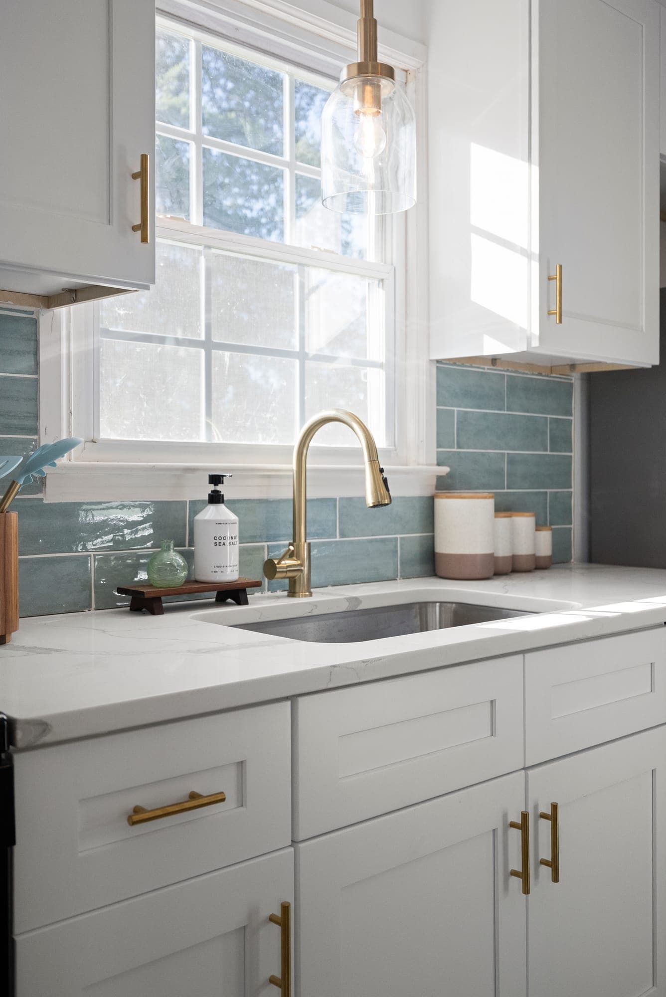 White shaker kitchen cabinets with brass pulls, quartz countertop and blue-green tile backsplash