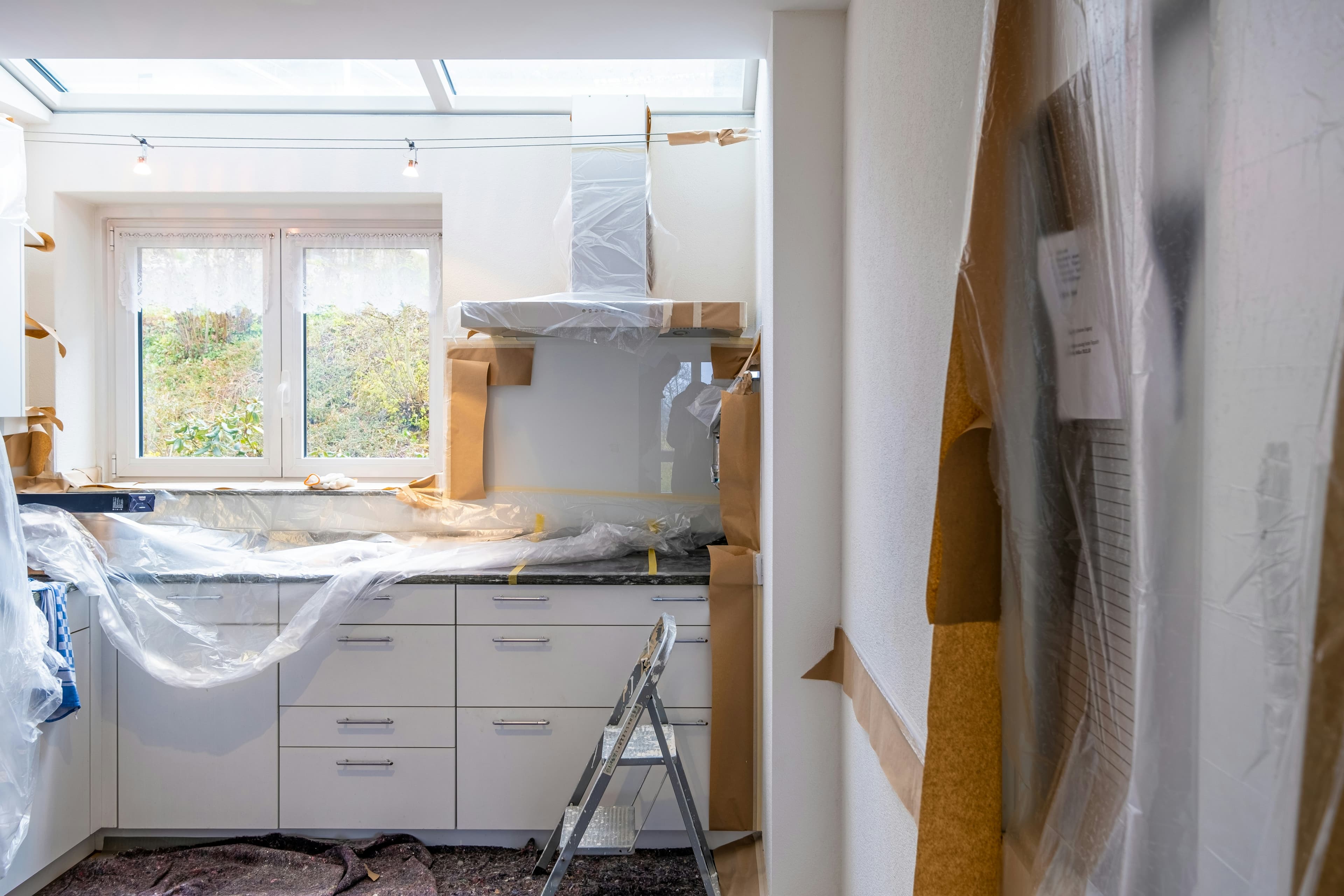 Kitchen mid-renovation with new white cabinets wrapped in plastic and paper