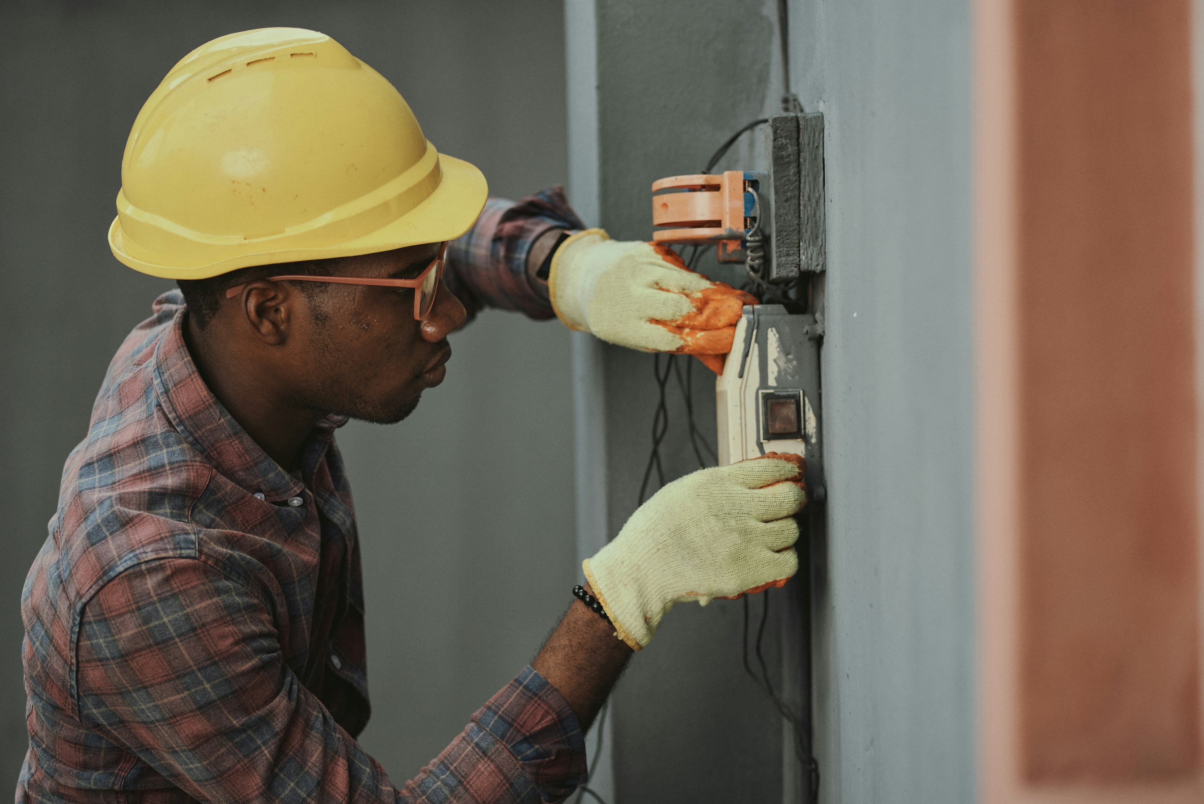 Electrician in a hard hat replacing a wall outlet