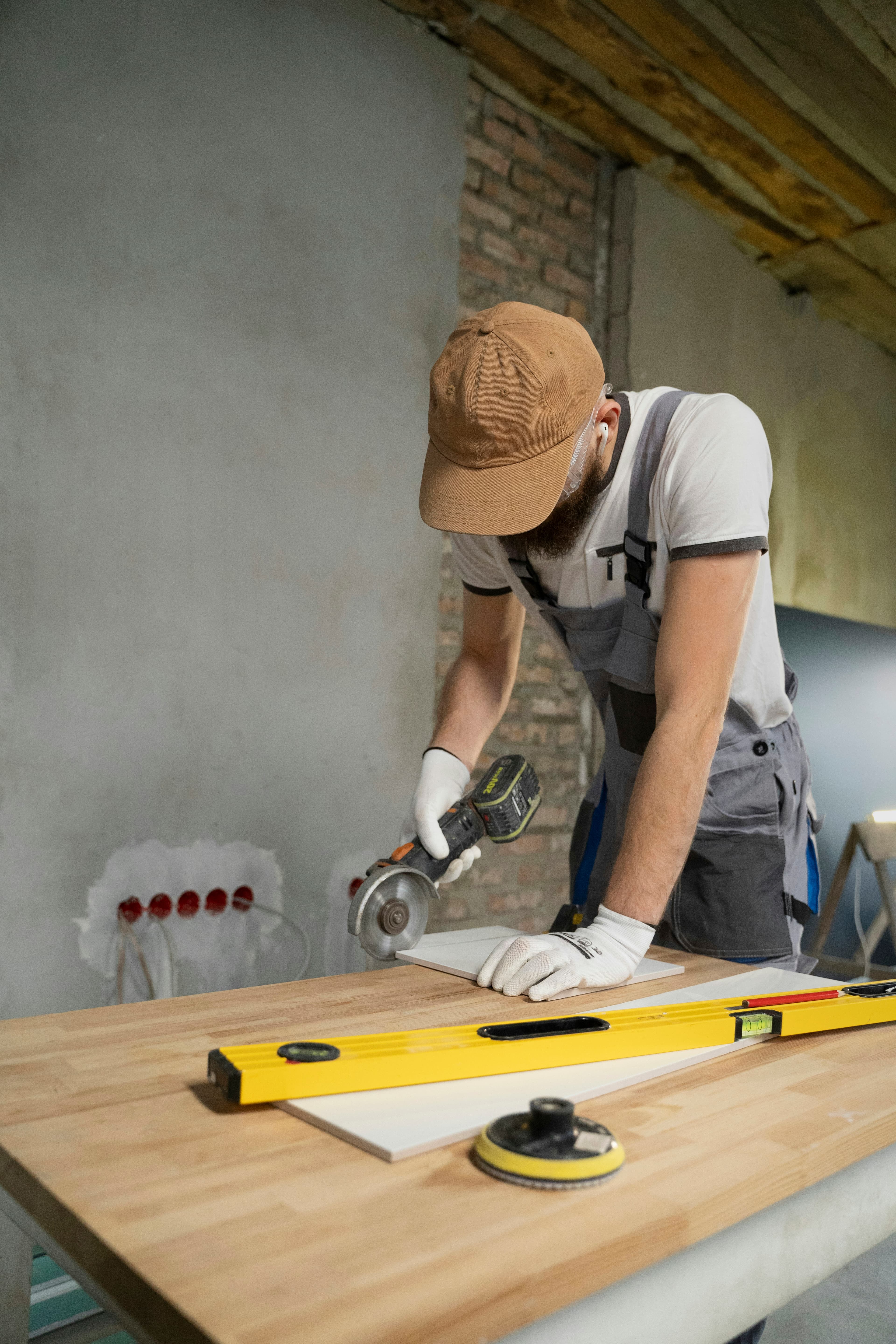 Installer in a cap and work gloves cutting a tile with an angle grinder
