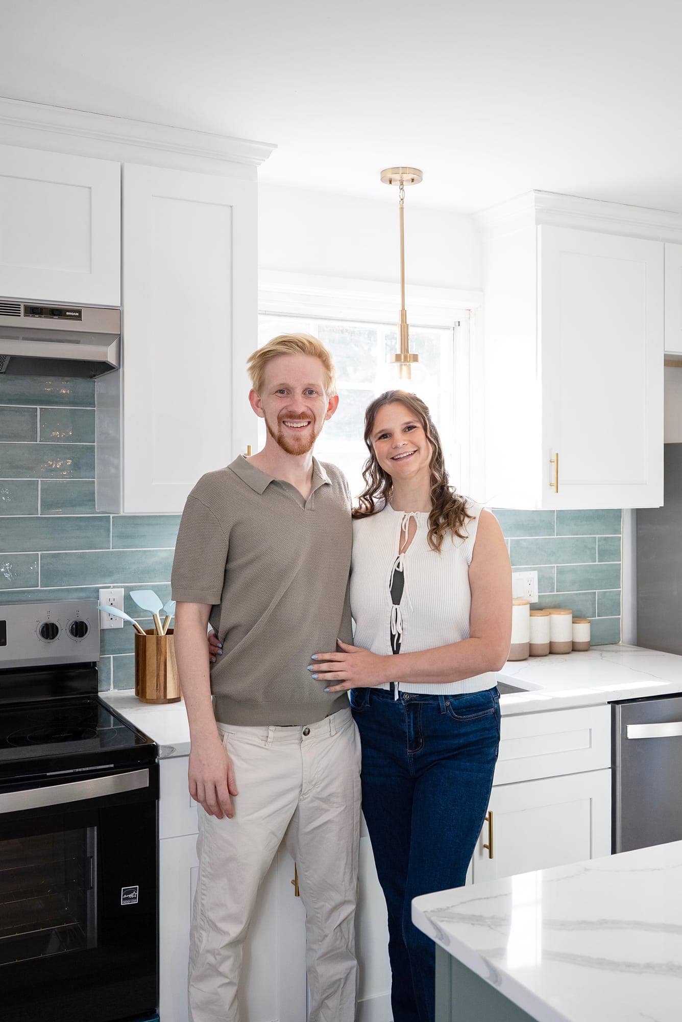 Mel and Scott, owners of The Punch Out Pros, in a finished kitchen with white cabinets and blue-green tile